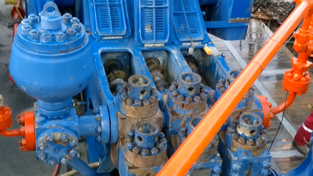 Close-up of a blue triplex mud pump used for drilling operations, showing its fluid end components and pistons.